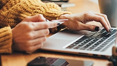 A close up of a woman reading her credit card to input the card number on her laptop keyboard.